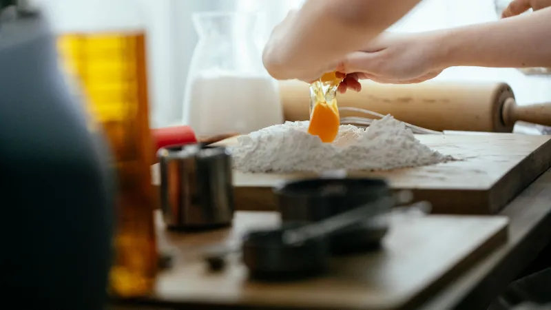 Kuchař rozklepává vejce do pšeničné mouky na dřevěném prkénku