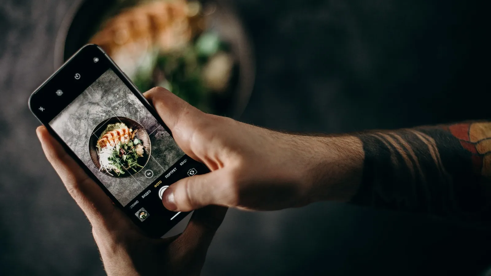 Hand holding a smartphone and photographing a plated dish on a dark table