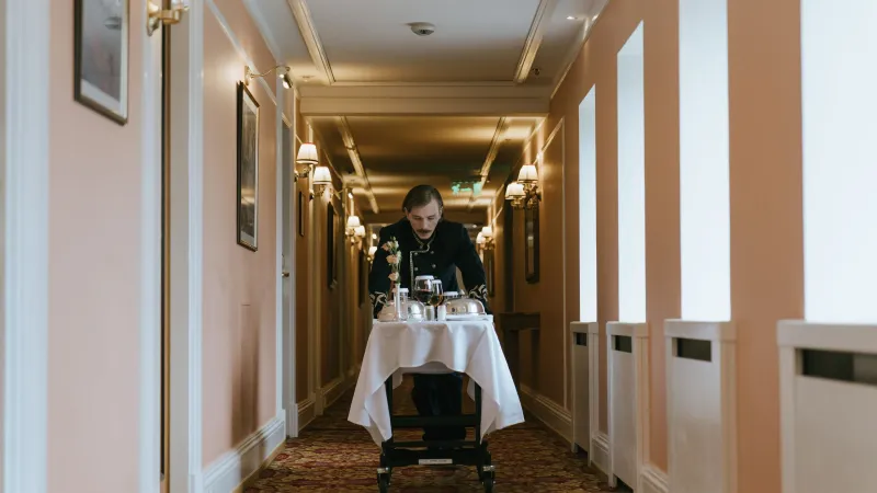 Hotel waiter pushing a room service trolley along a hotel corridor