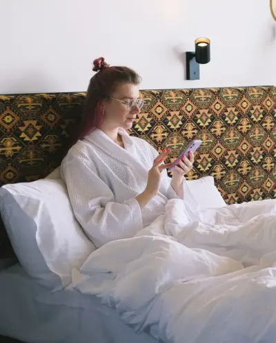 A guest in a bathrobe reads the room service menu on her phone in bed