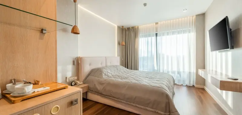 A quiet hotel room with a made bed and sheer curtains in daylight